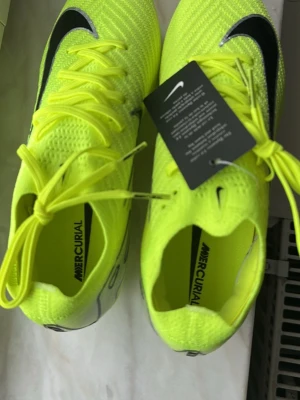 Nike Mercurial gula fotbollsskor - Säljer ett par Nike Mercurial fotbollsskor i neon-gult med svarta detaljer och klassisk Nike-logga. Skorna har snörning, stickad ovandel och genomskinlig sula med dobbar för bra grepp på planen. Perfekta för dig som vill sticka ut på fotbollsplanen.