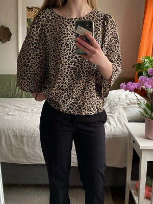 Leopardmönstrad blus med trekvartsärm - Snygg blus med leopardmönster i beige och svart. Modellen har rund halsringning och vida trekvartsärmar som ger en trendig siluett. Perfekt för dig som vill sticka ut med ett djurmönstrat plagg. Materialet känns lätt och luftigt.