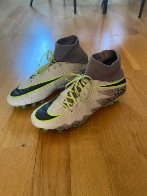 Nike Hypervenom Phantom 3 fotbollsskor - Säljer ett par Nike Hypervenom Phantom 3 fotbollsskor i vitt med svarta och neongröna detaljer. Skorna har högt skaft i grått tyg och snörning framtill. Yttermaterialet är syntetiskt med mönstrad struktur för bättre bollkontroll. 