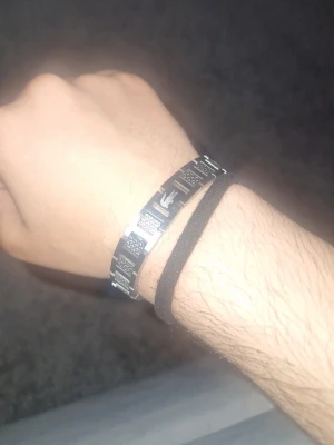 Lacoste armband - Snygg lacoste armband som jag har haft i ba 2 dagar. armband i silverfärgat rostfritt stål med rektangulära länkar och ingraverade mönster på varje länk. Armbandet har en stilren och modern design som passar perfekt till din vardagsstil.