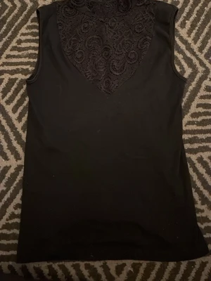 Svart ärmlös topp med spetsdetalj - Snygg svart ärmlös topp med turtle-neck och spets detalj upptill. Väldigt bra skick då den är använd fåtal gånger, tycker att tröjan är super fin men säljer då den tyvärr inte kommer till användning. Tveka inte på att höra av dig för fler frågor eller bilder🤗