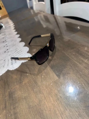 Svarta solglasögon med gulddetaljer - Stilrena solglasögon med svart båge och rektangulära glas. Snygga gulddetaljer vid skalmarna ger en exklusiv känsla. Perfekta för dig som vill ha en trendig accessoar med attityd.