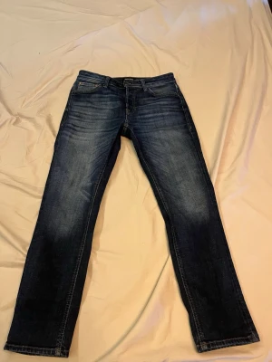Mörkblå  jeans från Jack and Jones - Säljer ett par mörkblå jeans från Jack and Jones  med klassisk femficksdesign och raka ben. Jeansen har snygga slitningar framtill och bakfickor med broderad detalj. Perfekta för en avslappnad och stilren look. Nypris ca 900 kr. Jättefint skick.