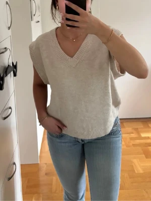 Stickad väst - Beige stickad väst med v-ringning från H&M. Västen har ribbade kanter vid hals och nederkant. Perfekt att styla över en skjorta eller T-shirt. Enkel och stilren design som funkar året om. 
