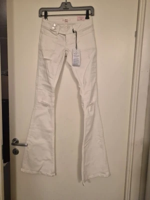Vita flared jeans från Gina Tricot - Säljer ett par vita flared jeans från Gina Tricot i modellen 'pleated flare jeans'. Jeansen har låg midja, dubbla knappar, stora fickor fram. Snygg utsvängd passform. Säljer de då de var för tajta.