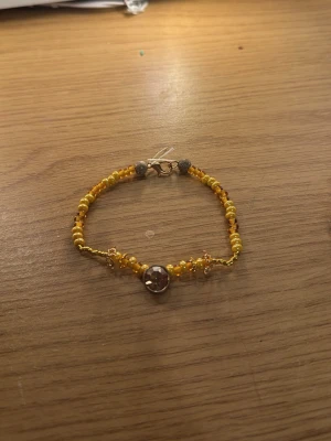 Två färgglada pärlarmband - Säljer två handgjorda armband med pärlor. Det ena armbandet har gula och orange pärlor med en liten blomdetalj i mitten. Det andra armbandet har pärlor i grönt, blått, rosa och turkost med en större pärla i mitten som har ett mönster. Båda har metallås.