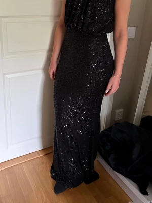 Svart glittrig balklänning  - Elegant svart långklänning med glittriga paljetter och halter neck. Klänningen är ärmlös sitter fint på kroppen samtidigt som man är bekväm. Perfekt för speciella tillfällen som bal och fest. Köpte för 3000 men säljer nu eftersom jag köpt en likadan fast i en annan färg, lappen är kvar och den är helt oanvänd!  