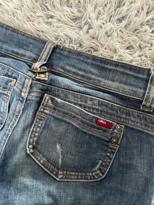 Blå bootcut jeans från Only - Säljer ett par blå bootcut jeans från Only med slitna detaljer och hål på benen. Jeansen har klassisk femficksdesign, låg midja och snygga slitningar för en cool look. Perfekta för dig som gillar en avslappnad och trendig stil.