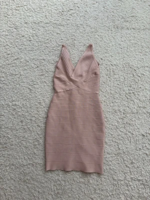 Beige rosa trendig bandage klänning! - Snygg ljus beige kortklänning med omlottdesign och v-ringning. Klänningen har breda axelband, markerad midja och dragkedja i ryggen. Tillverkad i ett stretchigt material som formar sig efter kroppen och ger en tight passform. Står storlek M men passar bäst på S/XS