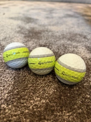 TaylorMade golfbollar med gul rand - Tre vita golfbollar från TaylorMade med en tydlig gul rand och svarta linjer runt om. Perfekta för dig som vill ha extra synlighet på golfbanan. Klassisk rund form och tillverkade i slitstarkt material. Skriv privat för pris och hur många