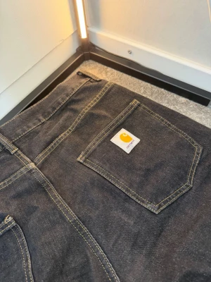 Vintage Svarta Carhartt Jeans - Snygga vintage svarta jeans från Carhartt med raka ben och klassiska kontrastsömmar. Jeansen har två bakfickor, varav en med Carhartt-logga, och är tillverkade i kraftig denim. Perfekta för en streetwear-look. Priset går absolut att diskuteras