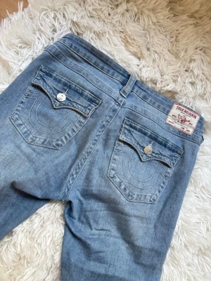 True Religion ljusblå bootcut jeans - Ljusblå jeans från True Religion med bootcut, använda några gånger, men inga hål eller liknande. Smått skadade längst ner, därav billigt pris.