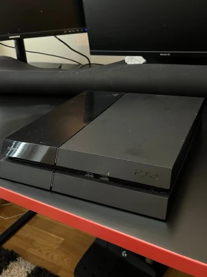 Sony PlayStation 4 spelkonsol svart - Säljer en svart PlayStation 4 från Sony. Konsolen har en stilren, rektangulär design med både matt och blank finish på ovansidan. Perfekt för gaming och streaming, passar snyggt in i alla setups.