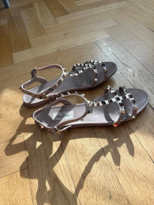 Valentino Garavani Rockstud Flat Rubber Sandaler - Säljer mina äkta Valentino Garavani puderrosa/beige rockstud sandaler i storlek 38. Använda endast ett fåtal gånger. De är gjorda i gummimaterial och är flexibla på fötterna. mycket snygga och de är i superfint skick, som nya. Tål vatten så perfekta även på stranden i sommar. Nypris mellan 4200-4700. Originallåda med dustbags och kort följer naturligtvis med. Upplevs som normala i storleken.