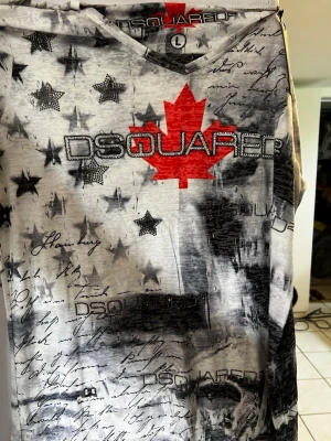 DSQUARED2 t-shirt med stjärnor och lönnlöv - Unik t-shirt från DSQUARED2 med svartvita stjärnor, handskrivna texter och ett stort rött lönnlöv på bröstet. T-shirten har v-ringning och coolt tryck både fram och bak. Perfekt för dig som vill sticka ut med en edgy och trendig stil.