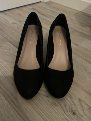 Svarta klassiska pumps från H&M - Stilrena svarta pumps från H&M med rundad tå och medelhög klack. Skorna har en matt finish och innersula i beige ton. Perfekta för dig som gillar en enkel och tidlös look.
