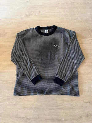 Randig långärmad tröja från polar - Säljer en svart och vit randig långärmad tröja från polar med broderad logga på bröstet. Tröjan har svarta ribbade muddar vid ärmslut och halsringning. Perfekt för dig som gillar en avslappnad och stilren look.