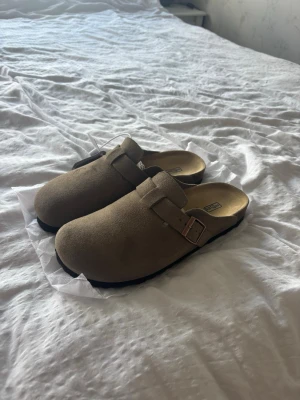Birkenstock Boston Clogs – Beige/Taupe  - Säljer dessa superfina Birkenstock Boston eftersom de tyvärr inte passade mig. Endast testade hemma i någon minut, annars helt oanvända och i jättefint skick. 🤍  * Storlek: 40 * Färg: Beige/Taupe * Skick: Som nya, aldrig använda ute * Med box följer tyvärr inte med  Perfekta inför sommaren och passar till allt – både casual och stilrent. Skitsnygga och väldigt trendiga just nu! ☀️  Hör gärna av dig vid frågor eller om du vill ha fler bilder 💌