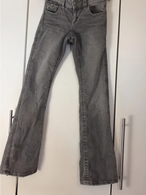 Grå bootcut jeans från Gina Tricot  - Snygga grå bootcut jeans med klassiska fem fickor och coola ficklock bak. Jeansen har låg midja och är tillverkade i denim med lätt tvättad look. Perfekta för en avslappnad och trendig stil.