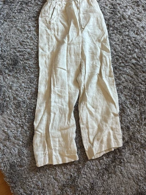 Beiga linnebyxor från arket - Snygga och luftiga linnebyxor från H&M i beige färg. Byxorna har resår i midjan med dragsko och raka ben. Perfekta för en chill och avslappnad stil. Gjorda i 100% linne för en skön känsla.