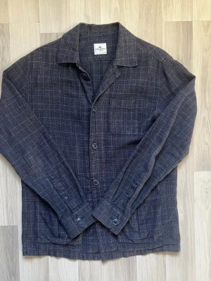 John Henric overshirt  - Säljer en riktigt snygg och mångsidig skjortjacka (overshirt) från John Henric. Ett perfekt plagg för övergångssäsonger eller att bära som ett stilrent lager över en t-shirt eller tunn tröja. Detaljer: • Märke: John Henric • Storlek: M (Medium) – Normal passform. • Färg/Mönster: Mörkblå bas med snyggt, subtilt rutmönster. • Skick: Väldigt fint skick, sparsamt använd och välvårdad.