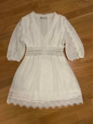   Ny slutsåld student Vit spetsklänning från Zara - Superfin vit kortklänning från Zara med v-ringning, spetsdetaljer och trekvartsärmar. Klänningen har vackra broderade spetskanter och markerad midja med spetsband. Perfekt för sommarens alla tillfällen!
