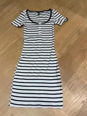 Randig kort klänning från H&M Divided - Snygg kortärmad klänning från H&M Divided i vitt med marinblå horisontella ränder. Modellen är kroppsnära med rund halsringning och knappar framtill. Perfekt för en avslappnad och trendig look.