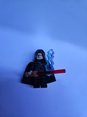 LEGO Star Wars minifigur med lasersvärd - Säljer en LEGO Star Wars minifigur med svart kåpa, tryckt dräkt och huva. Figuren har ett rött lasersvärd och blå blixtdel som tillbehör. Perfekt för samlare eller Star Wars-fans som vill utöka sin samling.