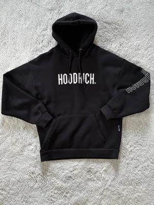 Hoodrich hoodie - Svart hoodie från Hoodrich med stor vit logga på bröstet och tryck på ena ärmen. Den är nästan helt oanvänd och kostar endast 120kr. Storlek är XS men passar S
