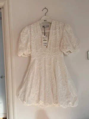 Vit studentklänning från Zara - Superfin vit kort klänning från Zara med puffärmar och v-ringning. Klänningen har broderade blommor över hela tyget och en lätt volangig kjol. Perfekt för dig som gillar romantisk och trendig stil. Köpte från vinted men tyvärr var den för liten för mig💓(Kolla gärna min profil, säljer även en annan jättefin studentklänning)🌷