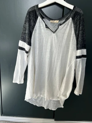Vit och grå långärmad topp - Vit och grå långärmad topp från Mulberry & Grand med kontrastfärgade ärmar och sportiga ränder. Toppen har v-ringning med dekorativ detalj och är tillverkad i ett mjukt, tunt material som känns skönt mot huden.