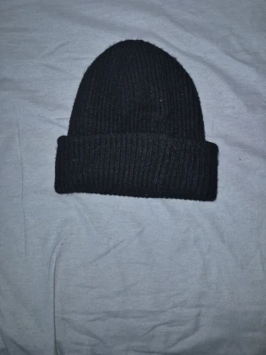 Svart ribbad mössa - Klassisk svart ribbad mössa med uppvikt kant. Perfekt för kalla dagar och enkel att matcha till alla outfits. Tidlös design som funkar året runt.
