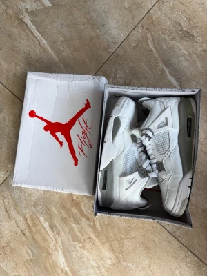  Air Jordan 4 Oreo sneakers - Snygga Air Jordan 4 Oreo sneakers i helvitt läder med meshpaneler och detaljer i grått. Klassisk siluett med högt skaft och ikonisk Jumpman-logga i rött på plösen. Perfekta för dig som vill sticka ut med stilrena och sportiga skor.