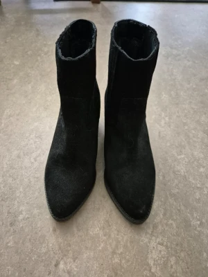 Boots - Snygga svarta boots i mocka med spetsig tå och medelhög klack. Modellen är klassisk och enkel, perfekt till jeans eller kjol. Materialet är mjukt och ger en lyxig känsla. Dragkedja saknas på sidan för en stilren look.