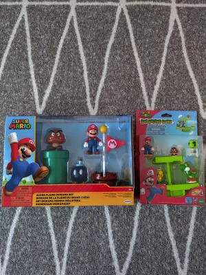 Super Mario dioramaset och balansspel - Två Super Mario-leksaker: ett Acorn Plains dioramaset med Mario, Goomba, rör, bomb och flagga samt ett Balancing Game med Mario och Goomba. Färgglada figurer i plast, perfekta för samlare eller Mario-fans.
