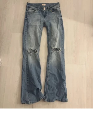 Low waist  bootcut jeans med hål - Säljer ett par ljusblå bootcut jeans med hål på. Dom har används fåtal gånger och tror inte dessa går att beställa på nellys hemsida längre nypriset är 699kr💕 Storlek S/36.