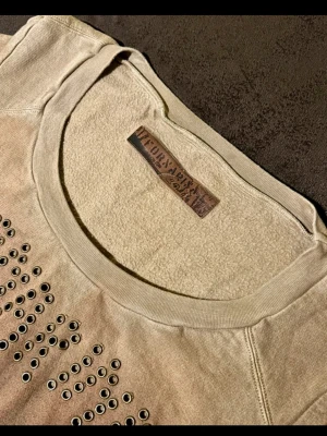 Vintage Fornari Studded Sweatshirt ✨ Y2K / Italian Designer - Säljer en unik beige sweatshirt från italienska Fornari (tidigt 2000-tal). Tröjan har en kaxig design med ett kors av nitar och textdetaljer framtill. Ett riktigt kap för dig som älskar autentisk Y2K-estetik! 🇮🇹 Mått & Passform: Bredd ca 50cm Bredd ca 40cm. Ärmlängd: ca 70cm. Storlek: L (passar bäst om du gillar en lite mer åtsittande eller "slim" vintage-look).