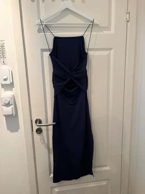 Marinblå långklänning med tunna band - Snygg marinblå långklänning med tunna axelband och draperad detalj framtill. Klänningen har en elegant, rak siluett och är perfekt för dig som gillar stilrena och trendiga plagg. Materialet känns mjukt och följsamt mot kroppen.