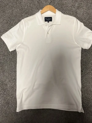 Vit pikétröja från Bondelid - Klassisk vit pikétröja från Bondelid med krage och knappar framtill. Tröjan är tillverkad i bomull och har korta ärmar. Perfekt för en clean och stilren look.