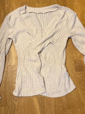 Ljusribbad omlottopp från SHEIN - Supersnygg ljus omlottopp från SHEIN i ribbat material. Toppen har lång ärm, v-ringning och figurnära passform. Perfekt att styla med jeans eller kjol för en trendig look.