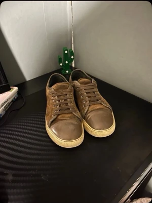 Bruna sneakers i mocka och läder - Snygga bruna sneakers med ovandel i mocka och detaljer i läder. Skorna har lågt skaft, rund tå och vita sulor. Perfekta för dig som gillar en klassisk och stilren look. Matcha med jeans eller chinos för en avslappnad vibe.