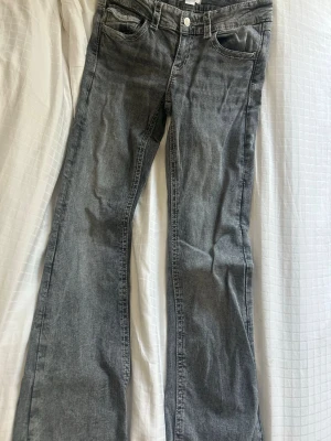 Grå bootcut jeans med fickor - Snygga grå jeans med bootcut-modell och klassiska fem fickor. Jeansen har silverfärgade knappar och detaljer på bakfickorna. Tillverkade i denim med en lätt tvättad look som ger en cool vibe.