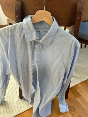 Blåvit randig skjorta från Zara - Snygg blåvit randig skjorta från Zara i regular fit. Skjortan har klassisk krage, knappar framtill och långa ärmar. Tillverkad i bomull, perfekt för en clean och avslappnad stil.