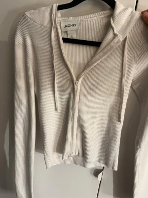 Vit ribbad hoodie från Monki - Säljer en vit ribbad hoodie från Monki i storlek XS. Hoodien har dragkedja framtill, långa ärmar och justerbar huva med snören. Perfekt för en avslappnad och trendig look.