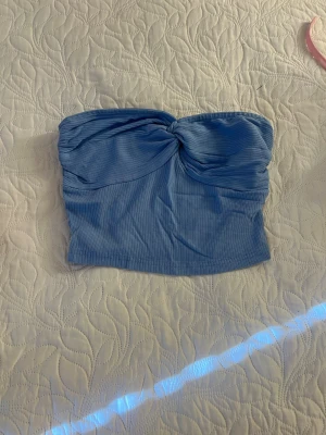 Blå ribbad bandeau tubtopp - Snygg blå bandeau tubtopp med twistad detalj framtill. Toppen är ribbad och har en croppad passform som passar perfekt till höga jeans eller kjol. Enkel att styla för en trendig look.