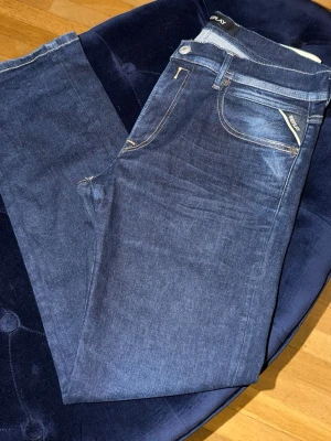 Mörkblå raka jeans från Replay - Snygga mörkblå jeans från Replay med raka ben och klassisk femficksmodell. Jeansen har kontrastsömmar och en liten Replay-logga vid fickan. Perfekta för en avslappnad och trendig look.31/32