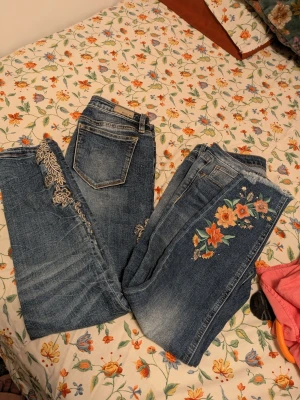 2 par Miss me jeans med broderade blommor - Säljer två par  blå jeans med snygga broderade blommor i vitt och färgglada toner längs benen. Jeansen har klassisk femficksmodell och raka ben. Perfekta för dig som vill ha en unik och trendig look med coola detaljer.