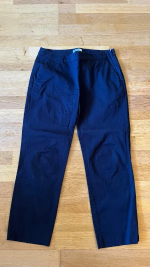 Mörkblå kostymbyxor  - Snygga mörkblå kostymbyxor med raka ben och diskreta sidofickor. Byxorna har en klassisk midja och är tillverkade i ett mjukt, vävt material som ger en clean look. Perfekta för dig som gillar stilrena och tidlösa plagg.