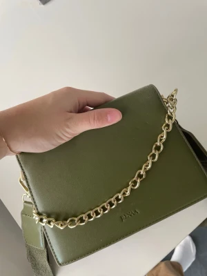 Väska från Jeenaa - Snygg väska från Jeenaa. Har 2 olika band (en guldkedja och ett grön länge band). Går att ta av båda. 