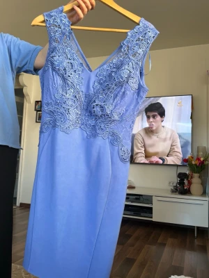 Ljusblå spetsklänning med v-ringning - Snygg ljusblå klänning med v-ringad hals och spetsdetaljer upptill. Klänningen är ärmlös och har en figurnära passform som ger en elegant siluett. Perfekt för dig som vill sticka ut med fina detaljer och fräsch färg.